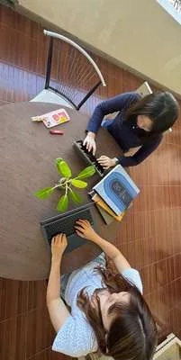 Dua anggota tim KriWul berdiskusi di meja dengan laptop dan catatan.