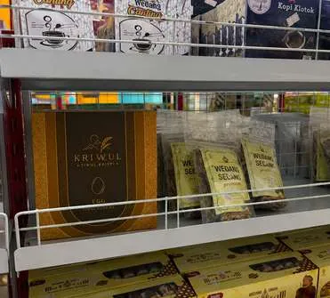 Anggota tim KriWul bersama staf toko memegang kotak KriWul di dalam toko oleh-oleh.