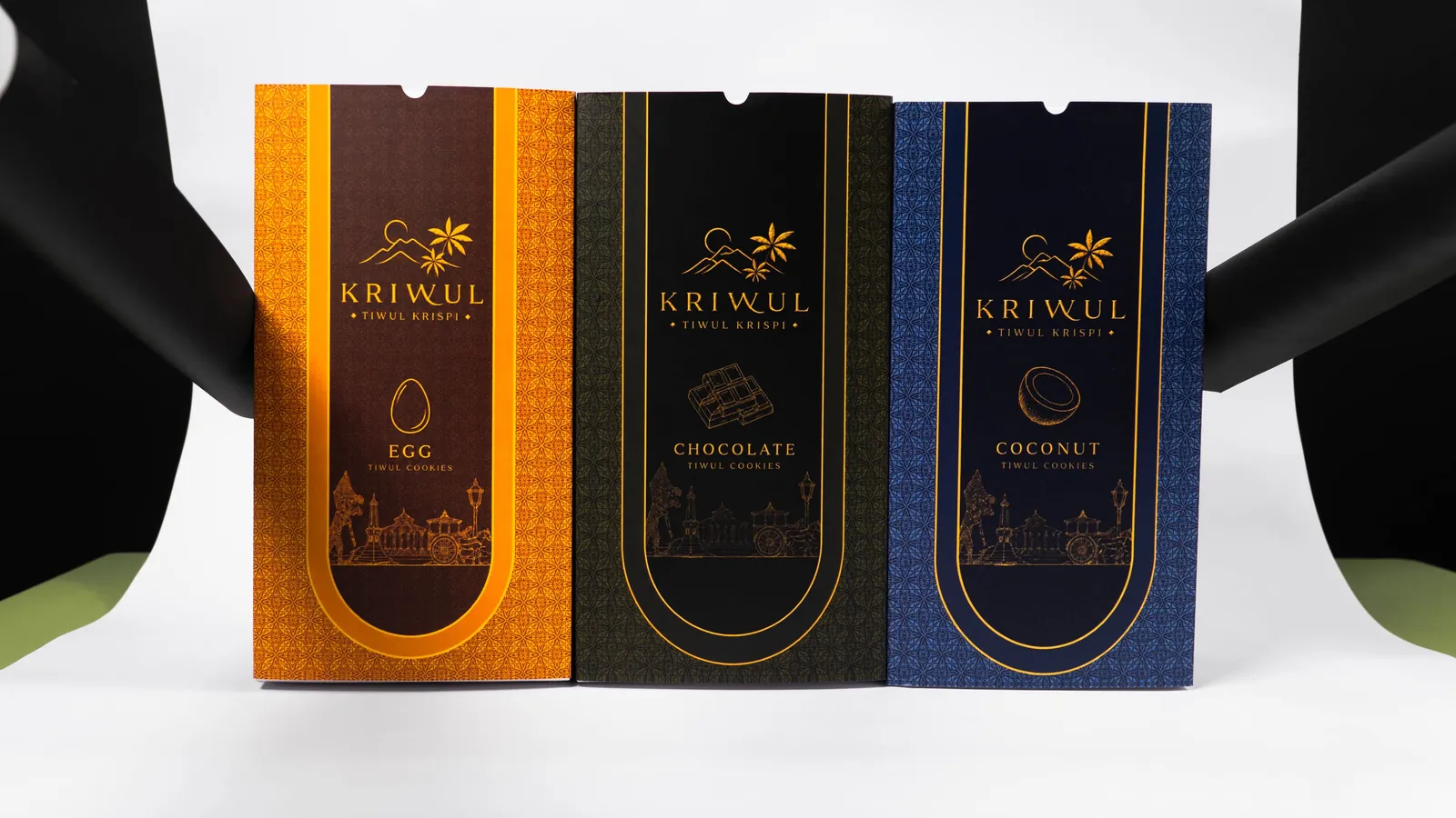 Tiga kotak KriWul berdiri berjajar: Salted Egg oranye, Chocolate hitam, dan Coconut biru tua, di depan latar gelap.